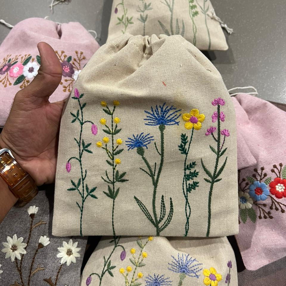 Embroidered fabric pouches with floral designs on a gray surface.